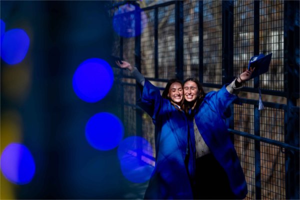  Students celebrate with graduation caps and gowns near blue lights.